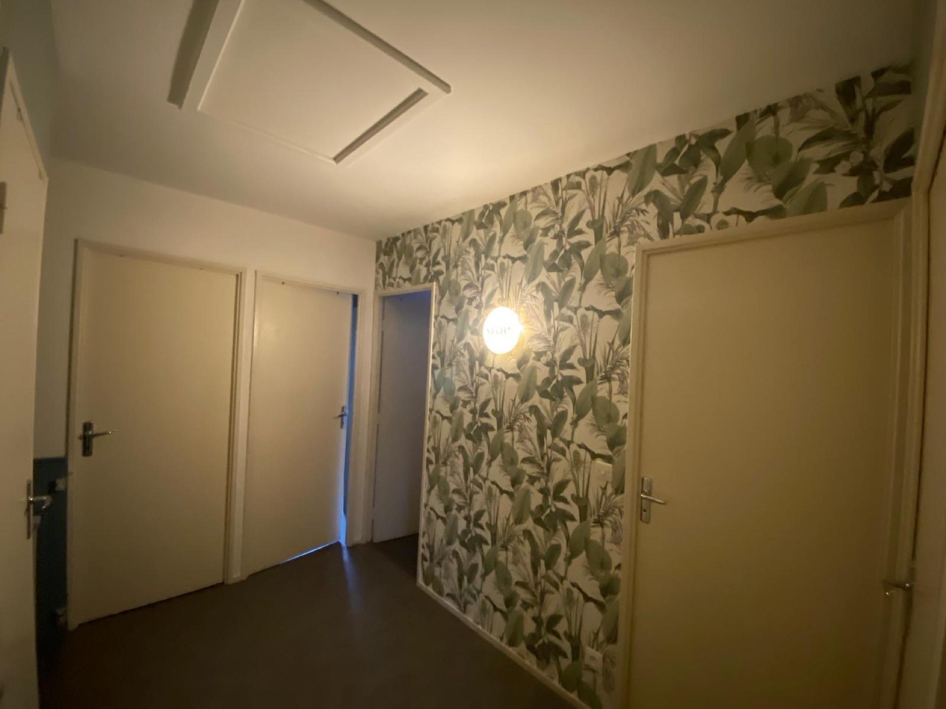 Détail d'une entrée avec papier peint à motif feuillage et menuiseries repeintes